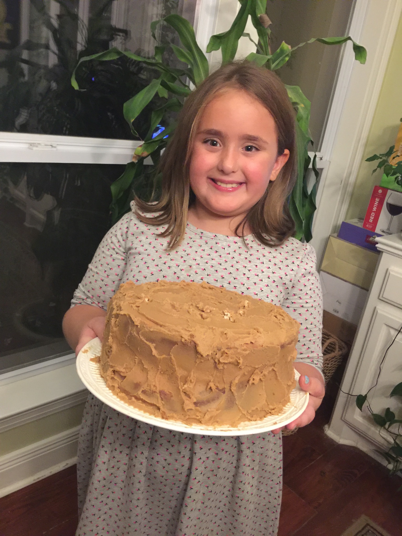 Little Lelia proudly holding a caramel-frosted cake on a big white plate